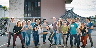 Junge Menschen halten Werkzeug in der Hand und stehen vor einem Gebäude, das renoviert wird.