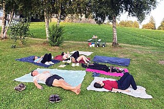 Jugendliche mit Gesichtsmasken liegen auf einer Wiese.