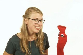 Deutsch mit Socke - Wie heißt du? Eine Frau hält eine rote Handpuppe in die Kamera und lächelt
