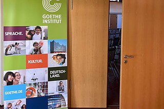 Ein Plakat des Goethe-Instituts und eine leicht geöffnete Türe.