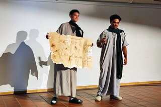 Zwei junge Männer in Gallabija halten ein Plakat mit Hieroglyphen in der Hand.