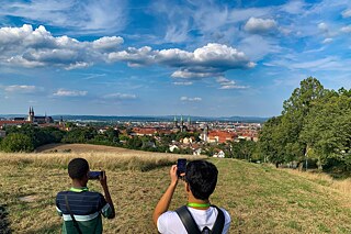 Jugendliche fotografieren Bamberg von einem Hügel aus.
