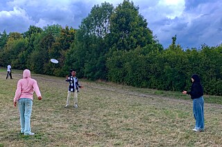 Jugendliche werfen eine Frisbeescheibe auf einer Wiese.