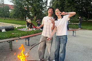 Zwei Jugendliche backen Stockbrot über dem Lagerfeuer.