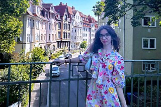 Junge Frau in einem geblümten Kleid steht auf einer Brücke. Im Hintergrund sieht man die Altstadt Göttingen.