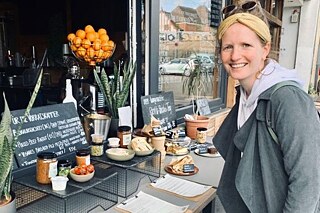 Frau steht vor einem Cafe und lächelt in die Kamera