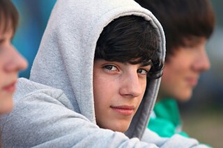 Ein Junge in einem grauen Hoodie mit Kapuze schaut in die Kamera