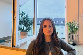 Eine Jugendliche mit langen Haaren sitzt vor einem offenen Fenster.