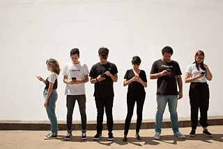 Sechs junge Menschen stehen nebeneinander und blicken konzentriert auf ihre Smartphones.