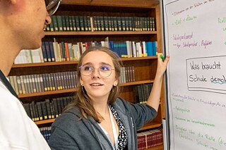 Eine Schülerin und ein Schüler stehen zusammen an einem beschriebenen Flipboard
