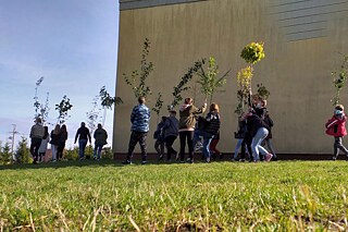 Schülerinnen und Schüler vor ihrer Schule tragen Bäume.