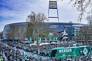 Werder Bremen-Bus auf dem Weg zum Stadion (im Hintergrund), von Menschen umringt