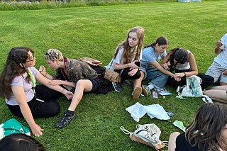 Jugendliche zeichnen Hennatattoos auf einer Wiese.