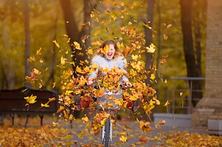 Eine junge Radfahrerin fährt durch umherwirbeldes, bunt gefärbtes Herbstlaub.