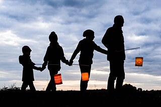 Ein Erwachsener und drei Kinder stehen in einer Reihe und halten leuchtende Laternen.