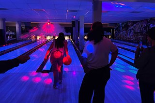 Jugendliche bowlen bei Neonlicht.