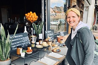Frau steht vor einem Cafe und lächelt in die Kamera