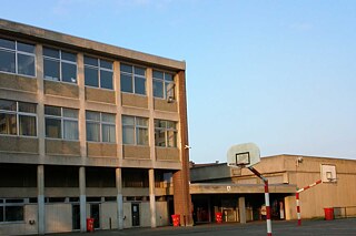 Gelbes Gebäude, im Vordergrund ein Basketballplatz mit Basketballkorb