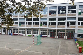 Weißes Schulgebäude mit Fussballplatz im Vordergrund