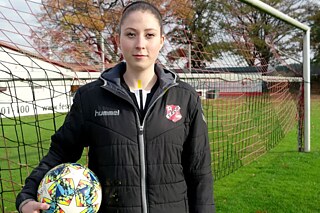 Mädchen in Sportkleidung mit Fußball in der rechten Hand vor einem Fußballtor