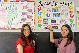 Zwei Schülerinnen stehen vor handgemalten Plakaten zum Thema Soziale Medien