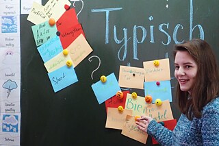 Mädchen steht an der Tafel mit Kärtchen über Deutschland und Deutsche