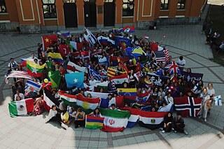 Eine große Gruppe von mindestens 100 Schülerinnen und Schülern mit Flaggen unterschiedlicher Nationen