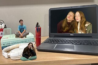 Schreibtisch mit Laptop, Büchern, Kopfhörern und zwei kleinen Figuren, die darauf platziert sind.