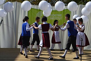 Schüler*innen tanzen in Tracht auf einer Bühne.