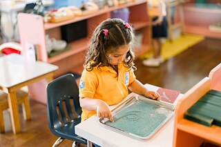 Ein kleines Mädchen sitzt alleine an einem Tisch und malt.