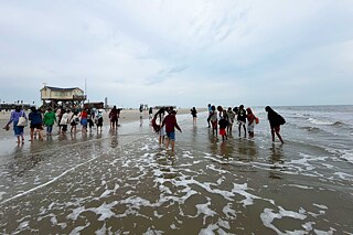 Jugendliche laufen an einem Strand durch das seichte Wasser.