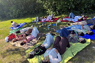 Jugendliche entspannen auf einer Wiese im Schatten.
