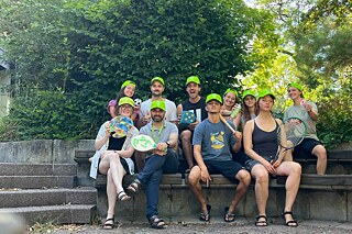 Eine kleine Gruppe junger Menschen trägt grüne Kappen und lächelt in die Kamera.