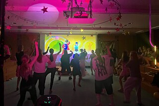 Jugendliche tanzen in einem mit buntem Neonlicht durchfluteten Raum.