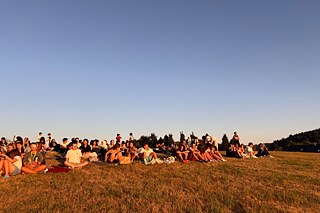 Junge Menschen sitzen auf einem Hügel und blicken in den Sonnenuntergang.