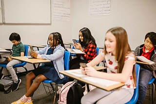 Junge Schülerinnen und Schüler in einem Klassenzimmer. Sie blicken auf Smartphones.