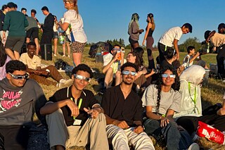 Junge Menschen sitzen auf einem Hügel, sie tragen Schutzbrillen und warten auf die Sonnenfinsternis.