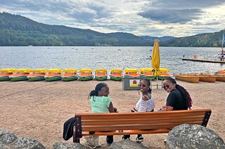 Drei Jugendliche genießen die Aussicht auf den Titisee von einer Parkbank aus.