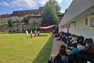 Jugendliche lauschen einem Vortrag im Freien.