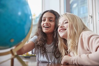 Zwei Mädchen sitzen im Klassenraum und sehen sich begeistert einen Globus an.
