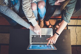 Personen sitzen vor einem Laptop.