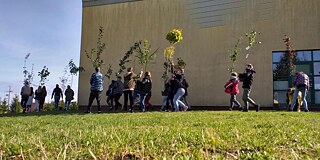 Schülerinnen und Schüler vor ihrer Schule tragen Bäume.
