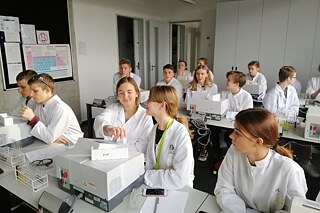 Schüler und Schülerinnen in einem Laborarbeitsraum in Schutzkleidung