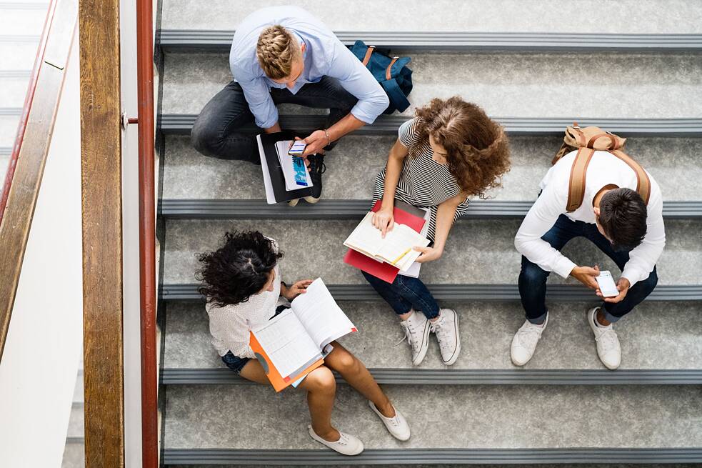 Studierende sitzen im Treppenhaus einer Hochschule