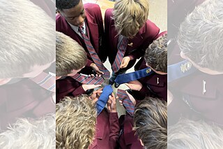 Eine Gruppe von Personen in einheitlichen Jacken hält mehrere gestreifte Krawatten in einem Kreis.