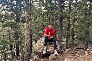 Ein junger Mann stitz auf einem großen Stein in einem Wald.