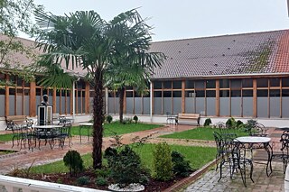 Das Bild zeigt den Innenhof einen Schule in der Türkei, die von dem deutschen Architekten Bruno Taut entworfen wurde. Es ist ein schöner Platz mit Pflanzen, der von einem Gebäude mit vielen hohen Fenstern umrandet ist.