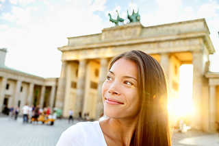 Eine junge Frau lächelt und guckt nach hinten über die Schulter, im Hintergrund steht das Brandenburger Tor.