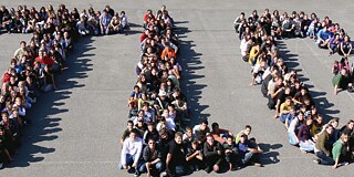 Gruppenbild, Schüler*innen formen Buchstaben der Schule