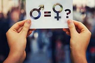 Zwei Hände halten einen Zettel mit den Zeichen für männlich und weiblich